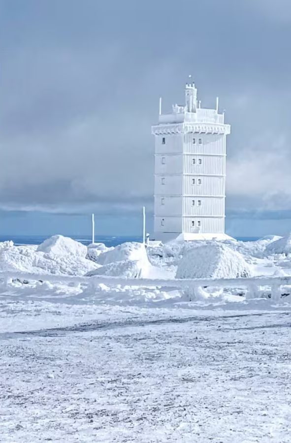 Ein hoher, weißer Turm steht in einer verschneiten, winterlichen Landschaft.
