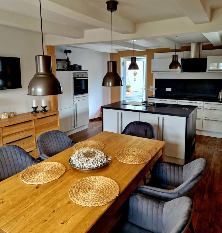 Moderne Küche mit Holz-Essbereich, Pendelleuchten und großen Fenstern.